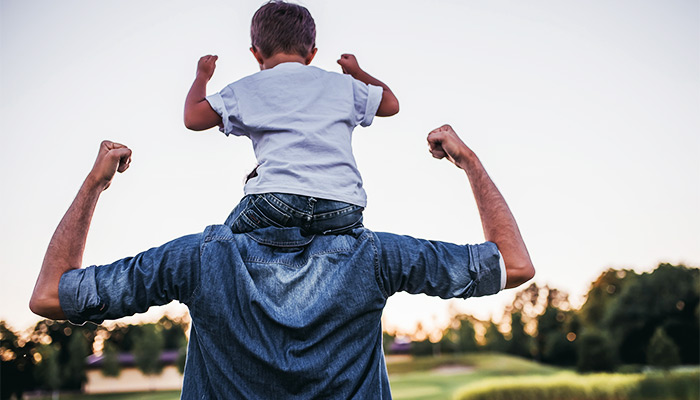 Dad flexing with his son on his shoulders at the park