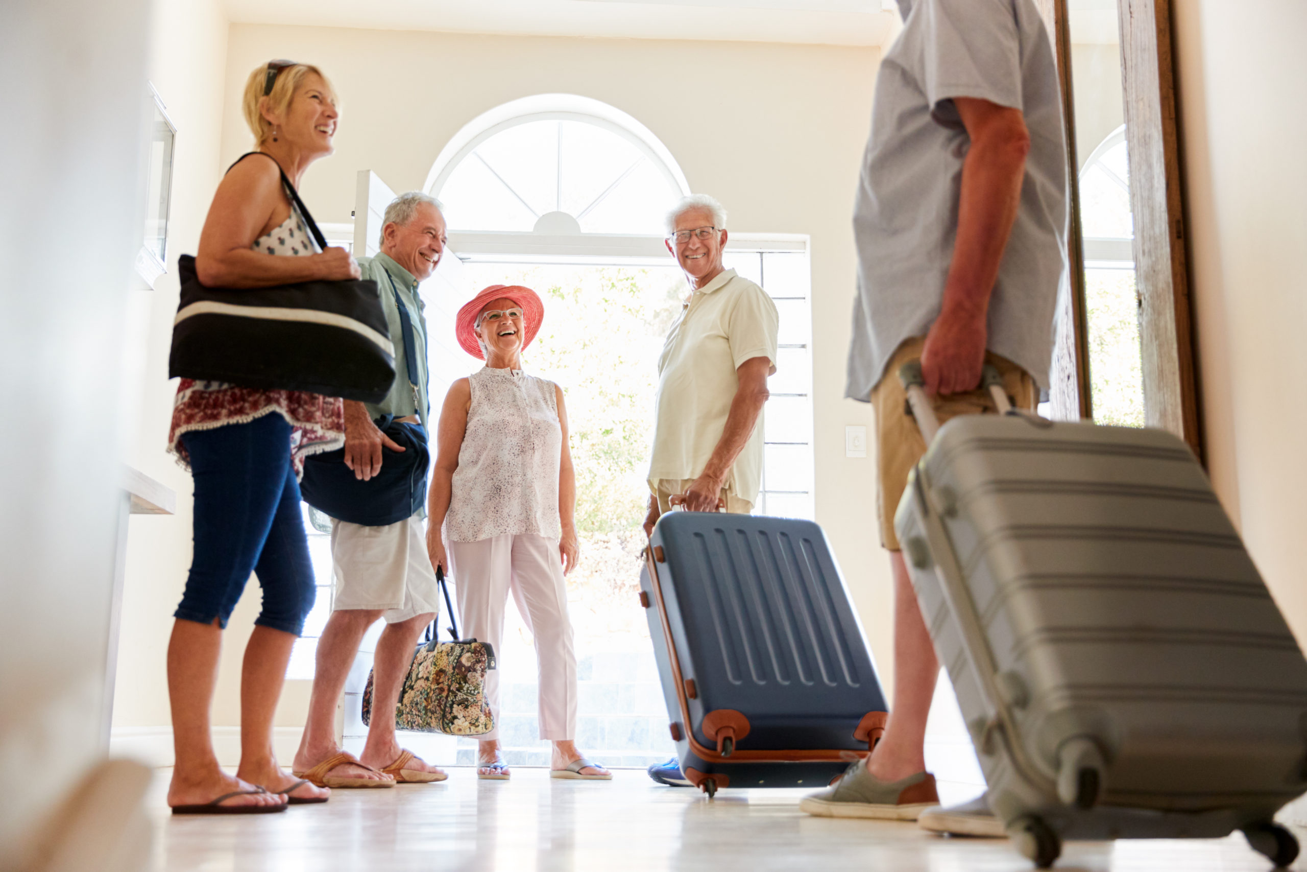 Group Of Senior Friends Standing By Front Door With Luggage About To Leave For Vacation Couple Painting House